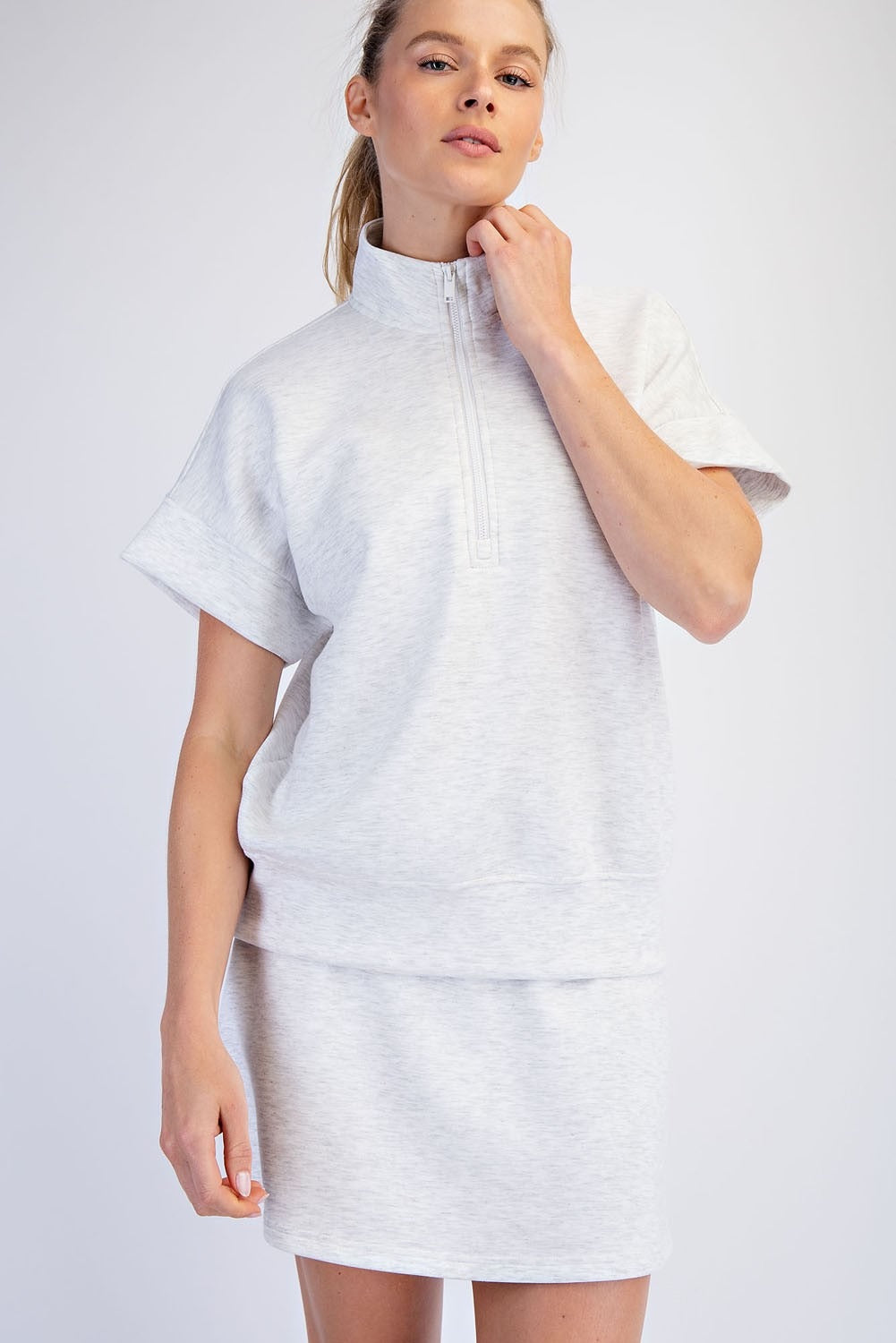 Person wearing a light gray short-sleeve top with a high collar on a white background