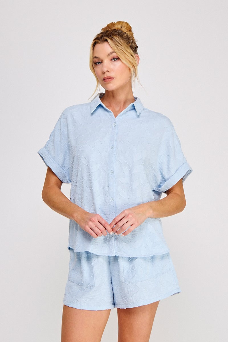 Woman wearing a light blue shirt and shorts set on a plain background