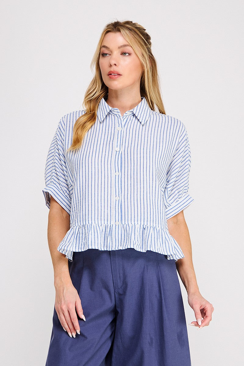 Woman wearing a blue and white striped shirt with ruffled sleeves on a plain background