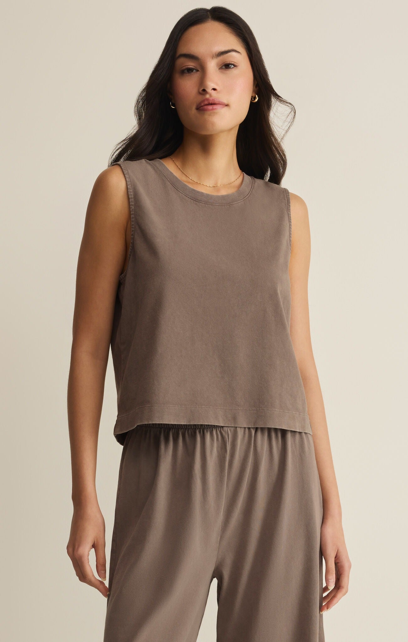 Woman wearing a brown sleeveless top and pants against a beige background
