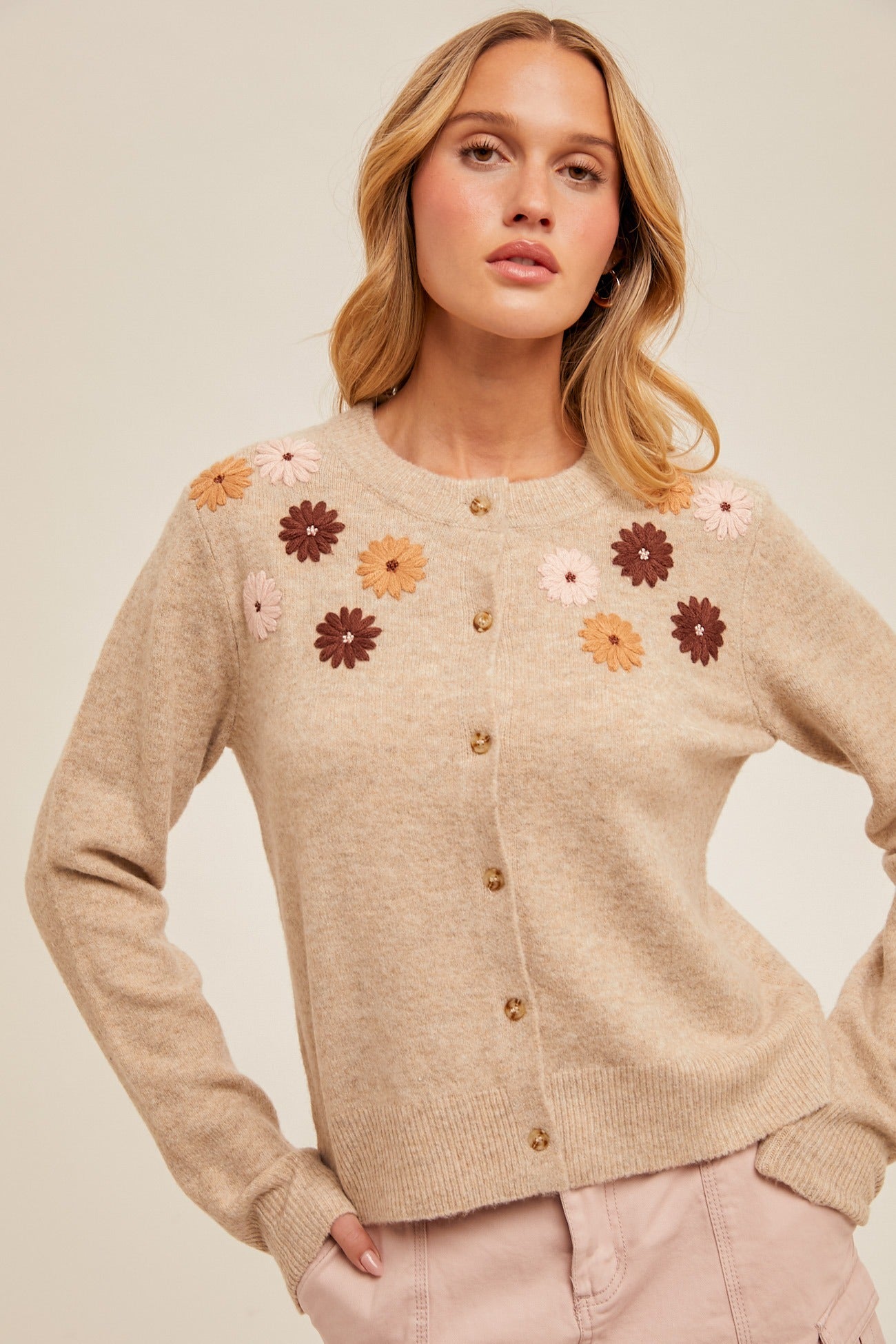Woman wearing a taupe sweater with floral patterns on a plain background