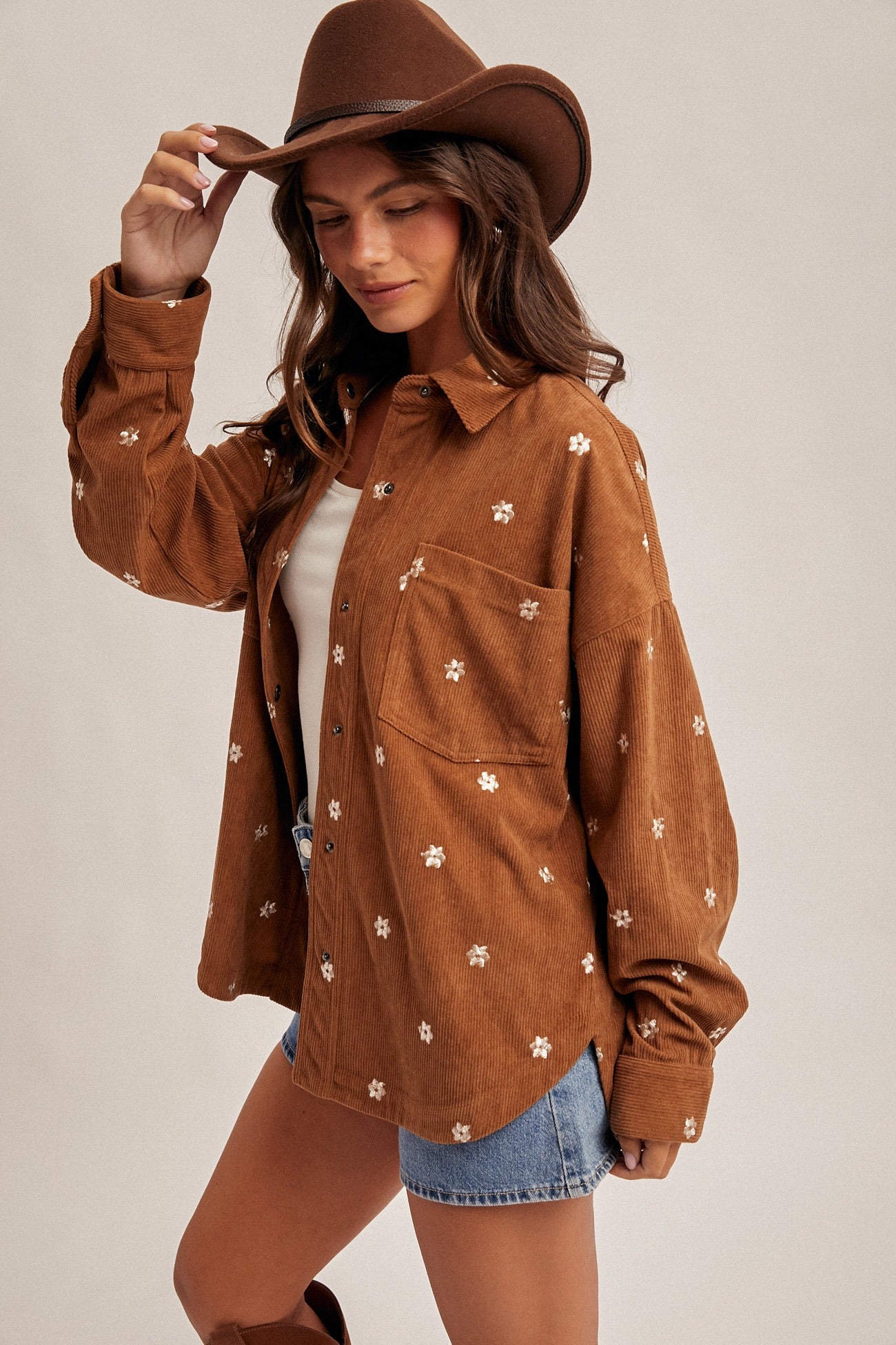 Woman wearing a brown floral-patterned shirt and cowboy hat on a plain background