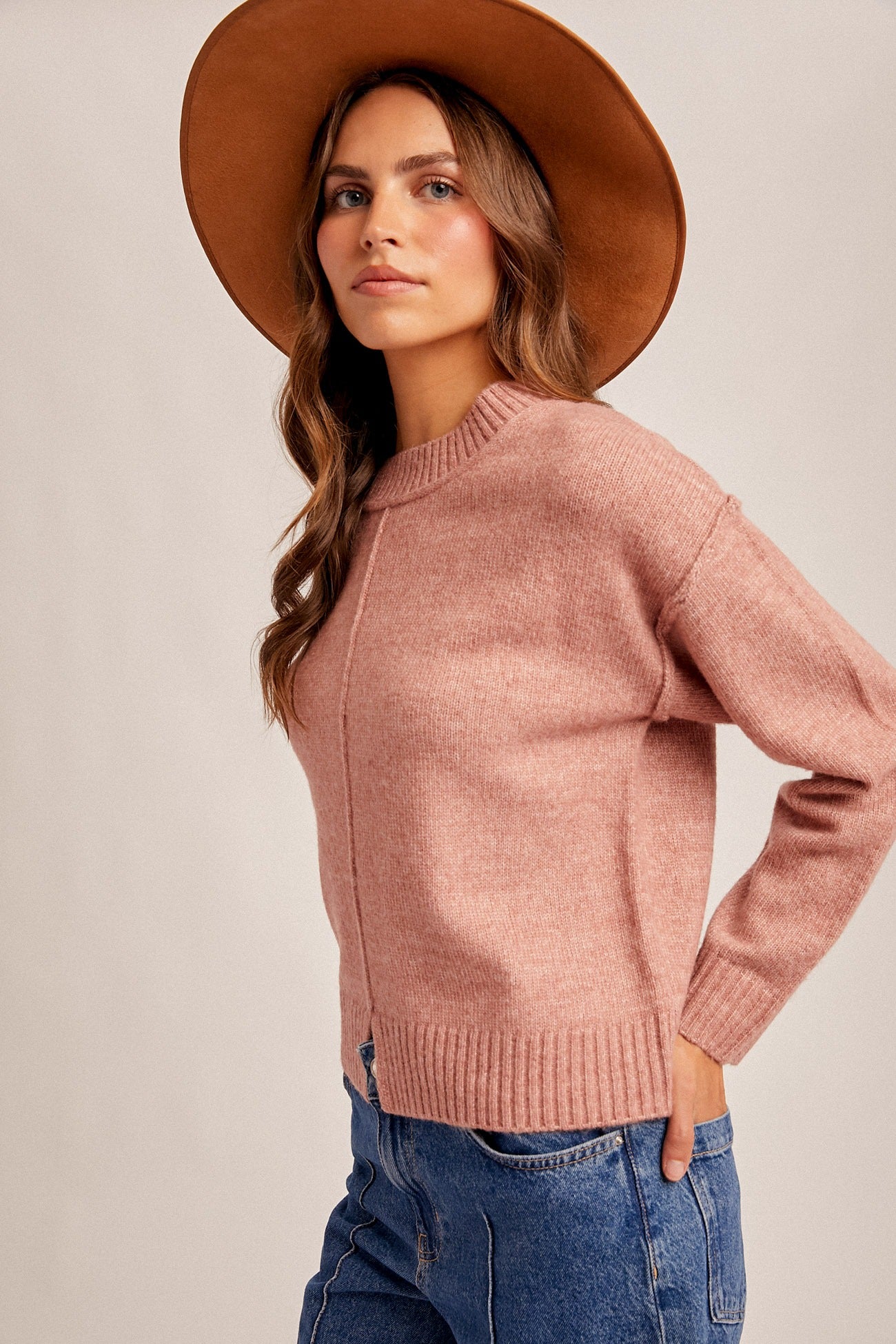 Woman wearing a pink sweater and brown hat against a beige background