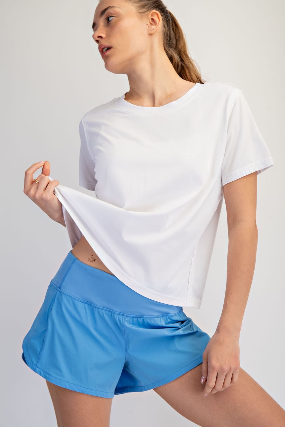 Woman wearing a white t-shirt and blue shorts on a plain background