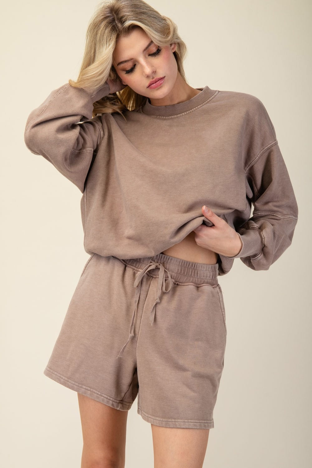Woman wearing a brown sweatshirt and shorts set on a beige background