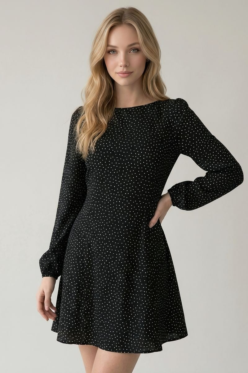 A woman modeling a black long-sleeve fit-and-flare dress with a small white polka dot pattern against a light gray studio background.