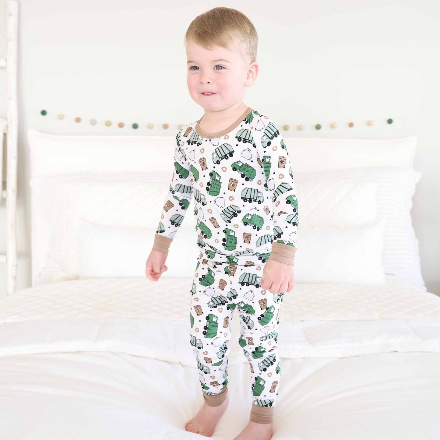 Child wearing a pajama set with green truck pattern on a white background