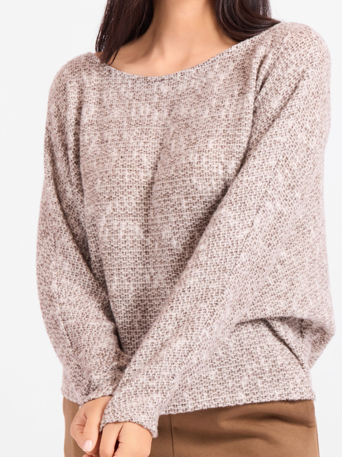 A woman wearing a fuzzy knit long-sleeve sweater in a heathered taupe-beige color, paired with brown pants, against a plain white background.