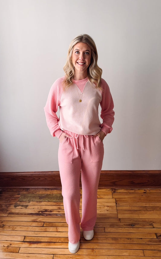 Woman wearing a pink outfit standing on a wooden floor with a white wall background