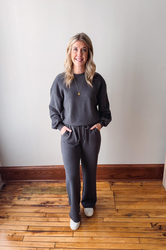 Woman wearing a gray outfit standing on a wooden floor with a white wall background