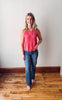 Woman wearing a pink top and blue jeans standing on a wooden floor against a white wall.