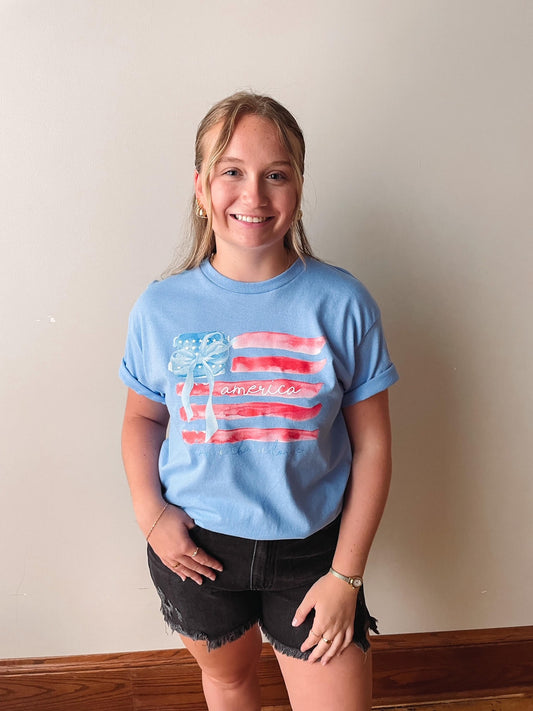 Person wearing a blue t-shirt with an American flag design against a plain wall.