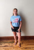 Woman wearing a blue t-shirt with an American flag design, standing against a plain wall.