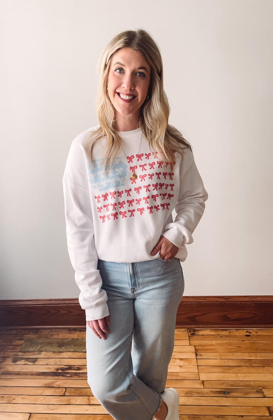 A person wearing a white sweatshirt with a pattern of the American flag made up of bows