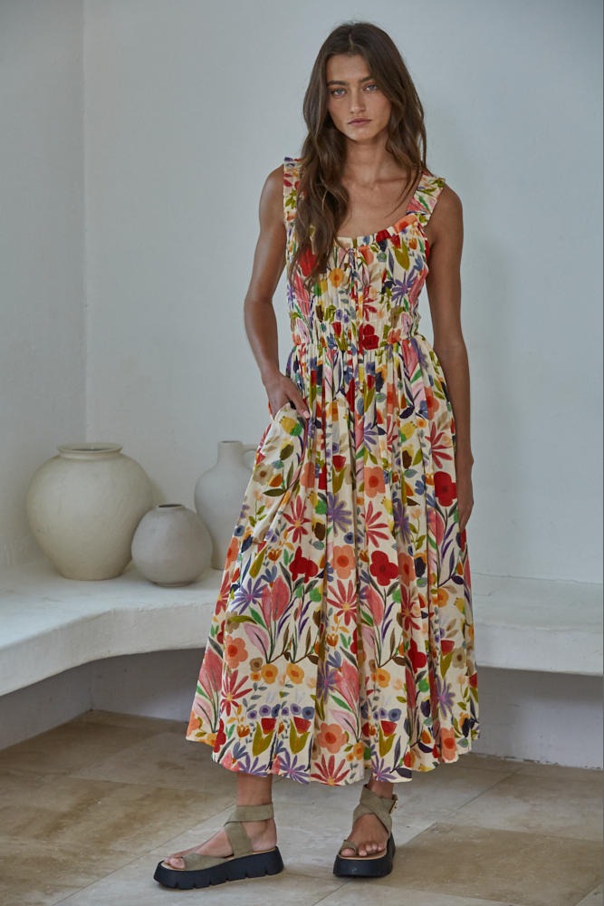 Woman wearing a colorful floral dress standing in a minimal indoor setting.