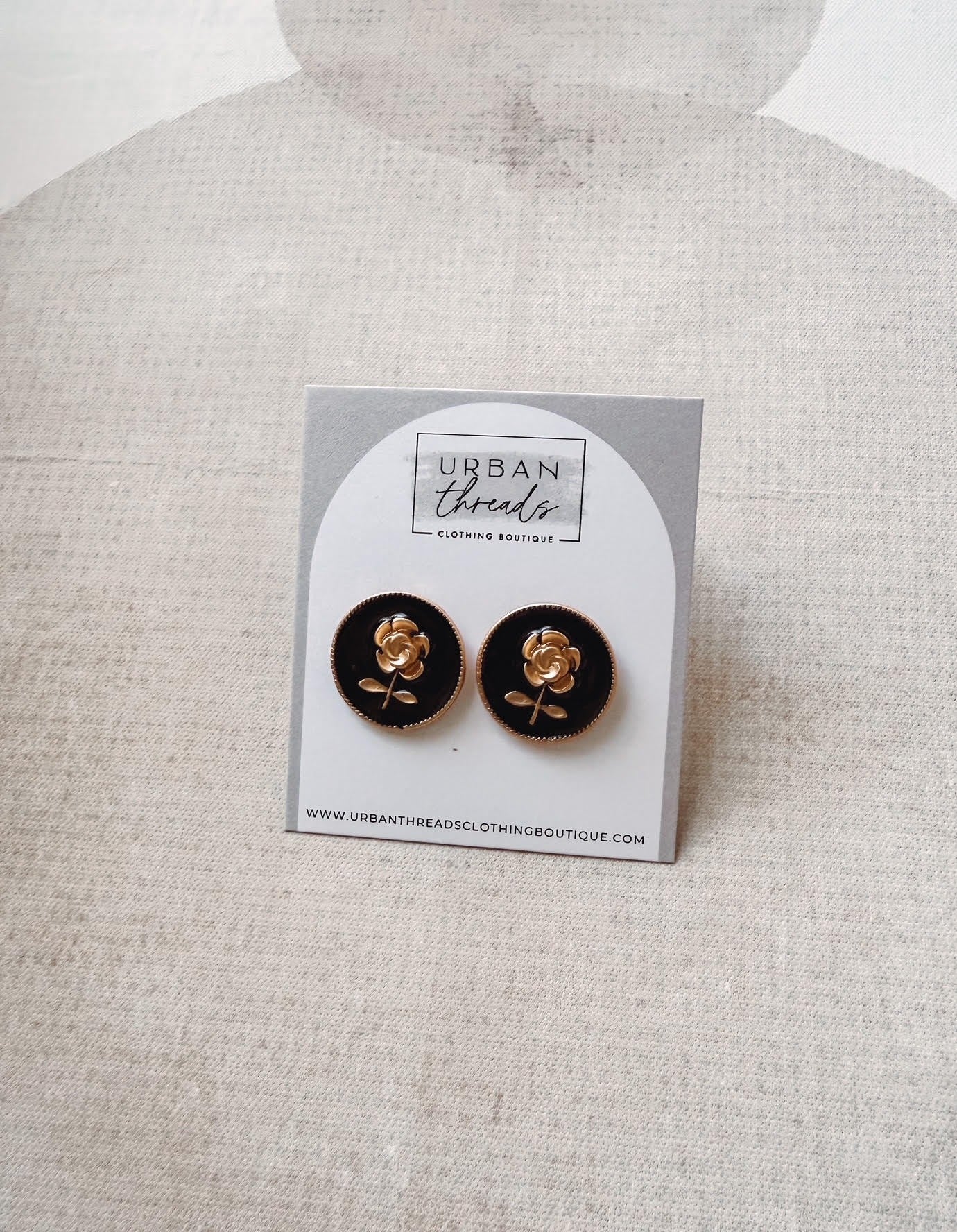 Black earrings with gold accents on a card labeled 'Urban Threads' against a light gray background