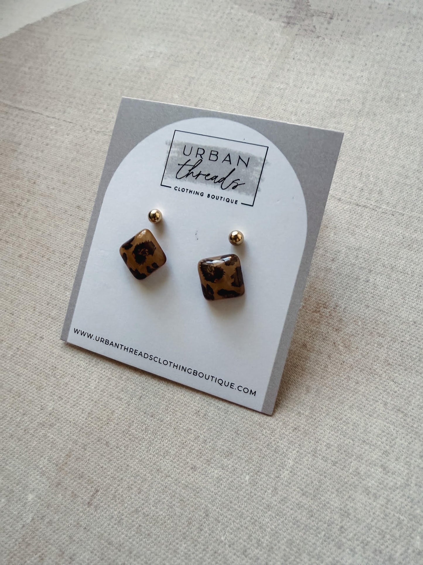 Pair of leopard print earrings on a branded card with 'Urban Threads' on a beige background