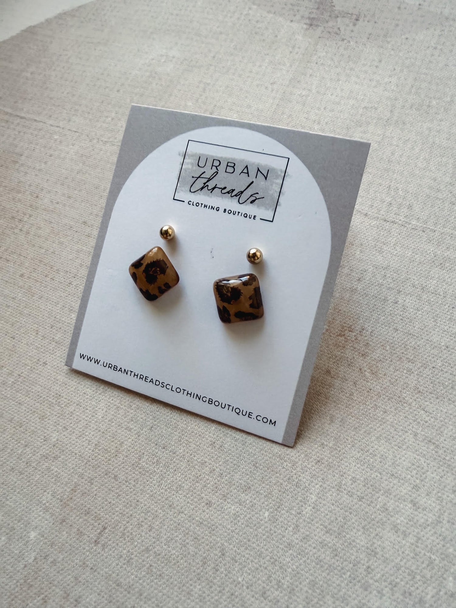 Pair of leopard print earrings on a branded card with 'Urban Threads' on a beige background