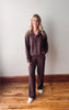 Woman wearing a brown outfit standing on a wooden floor against a white wall