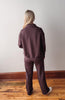 Person wearing a brown tracksuit standing on a wooden floor with a white wall background