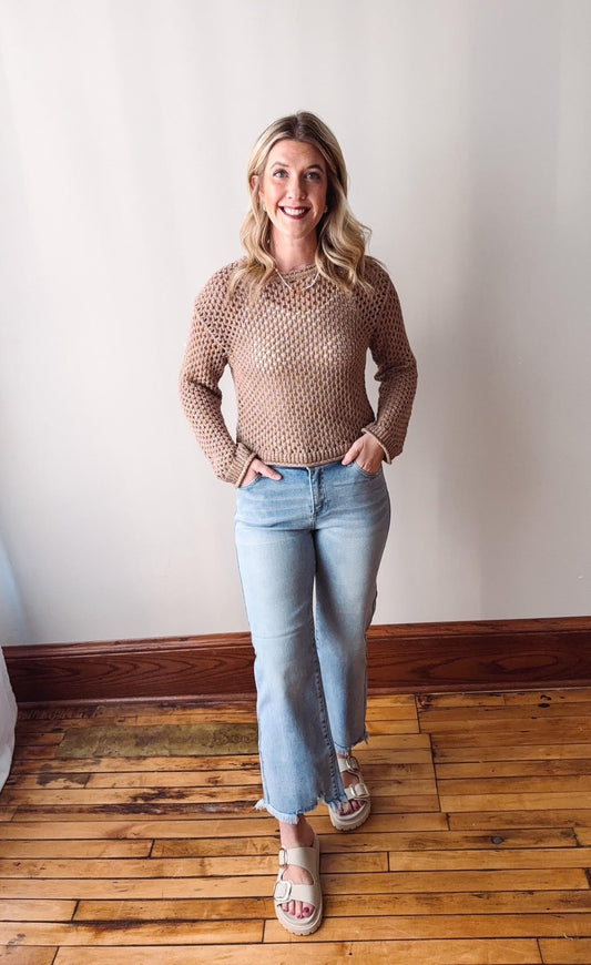 Woman wearing a beige sweater and light blue jeans standing on a wooden floor.