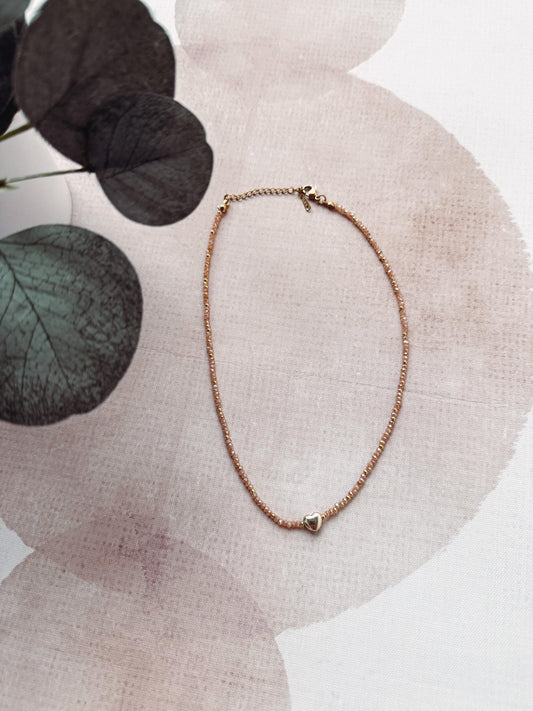 Rose gold necklace on a textured surface with floral elements