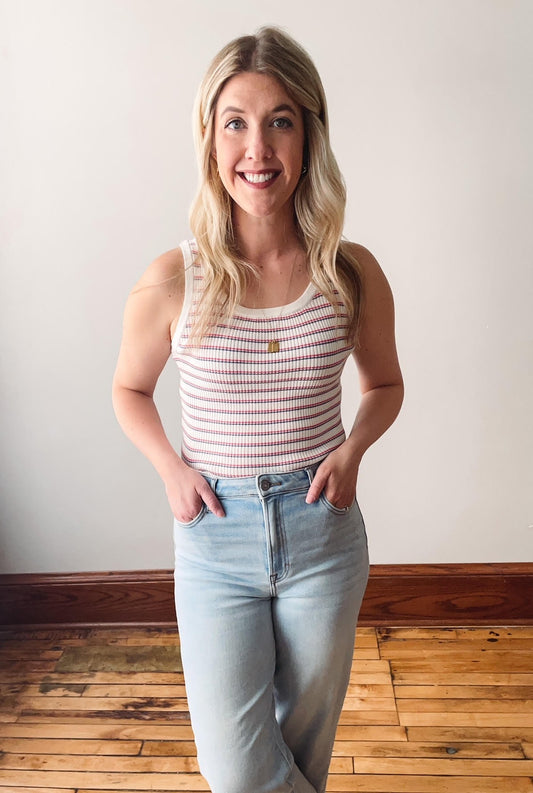 A person wearing a red and white striped ribbed tank top and light blue jeans, standing against a neutral background.