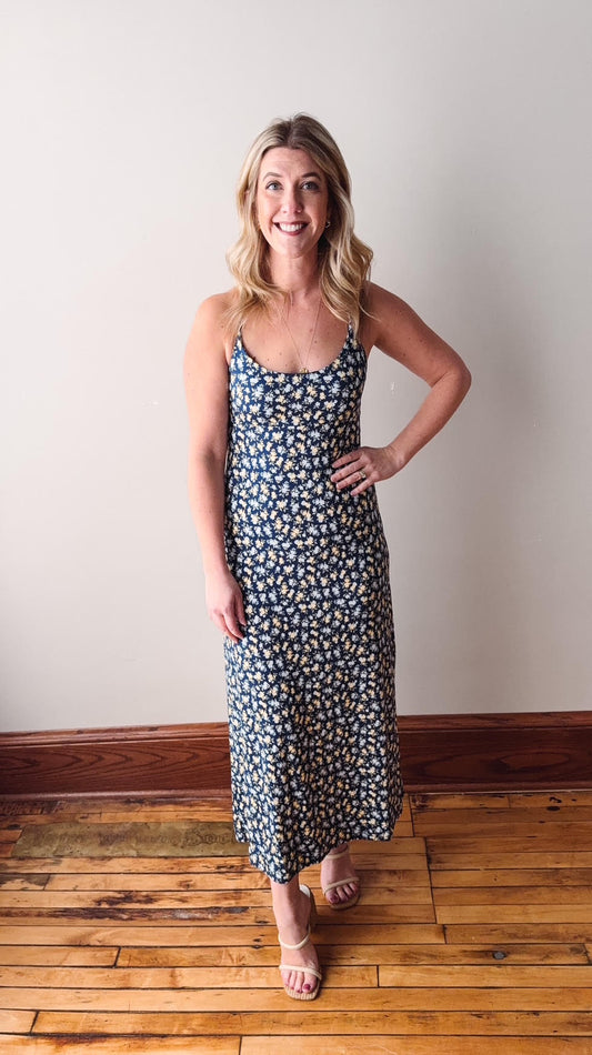 Woman wearing a floral dress standing on a wooden floor with a plain wall background
