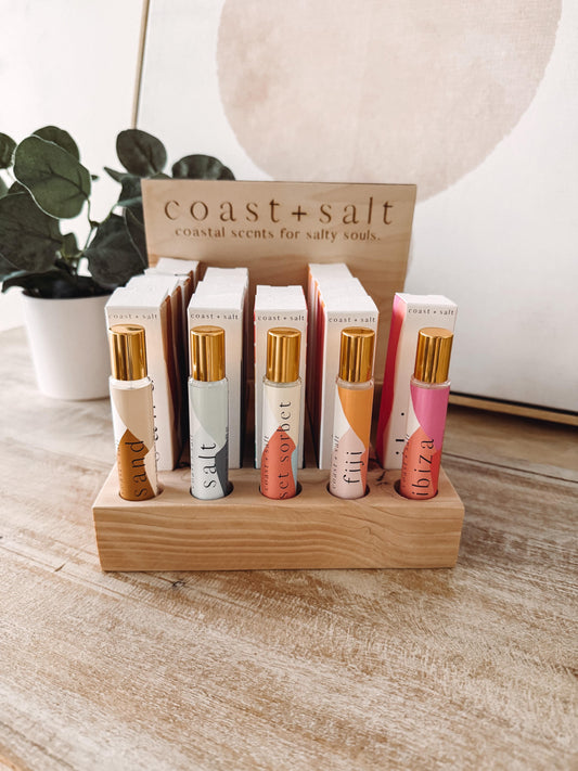 Collection of coast + salt perfume bottles on a wooden stand with a plant and lamp in the background.