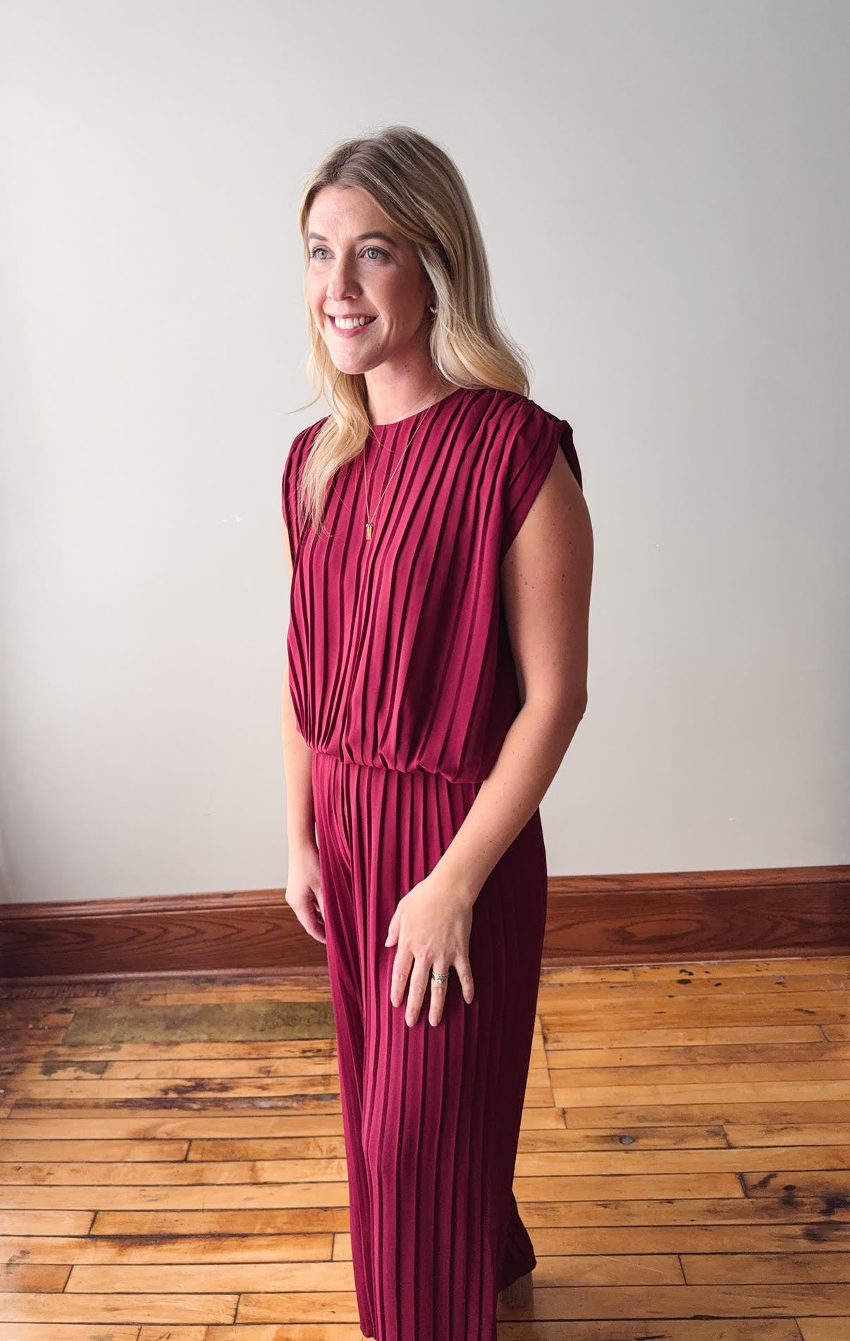 Woman wearing a burgundy dress standing on a wooden floor with a white wall background