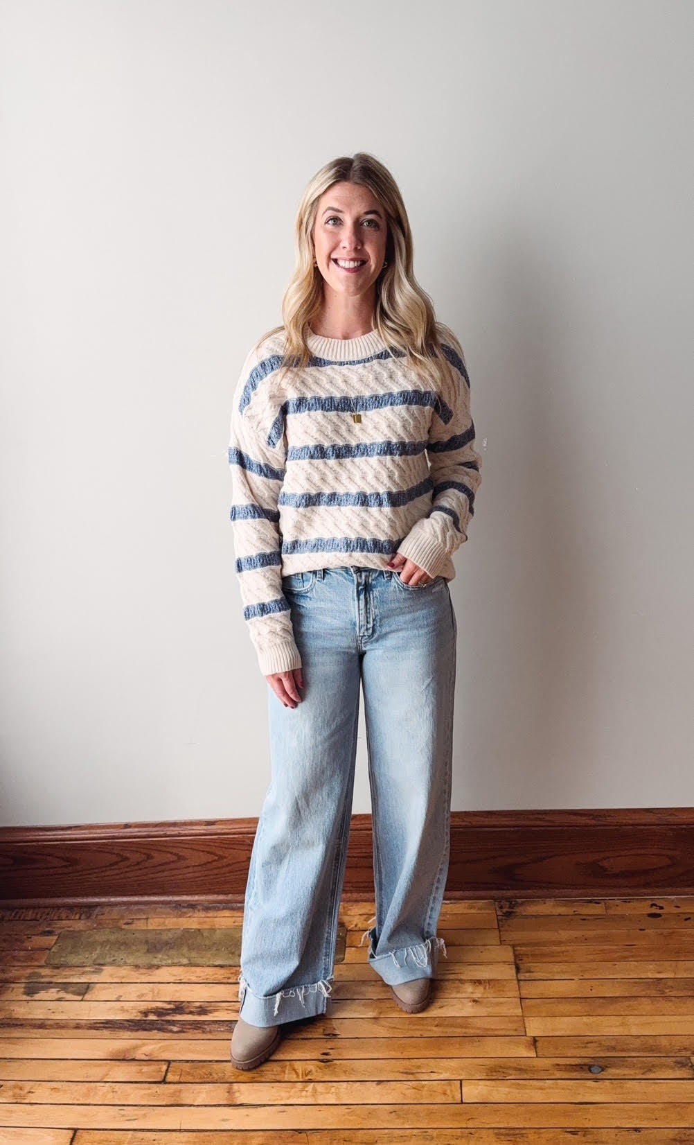 Woman wearing a striped sweater and jeans standing against a plain wall.