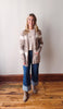 Woman wearing a striped cardigan and jeans standing on a wooden floor with a white wall background