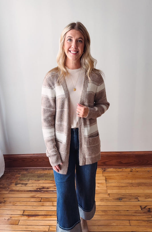 Woman wearing a striped cardigan and jeans standing in a room with wooden flooring.