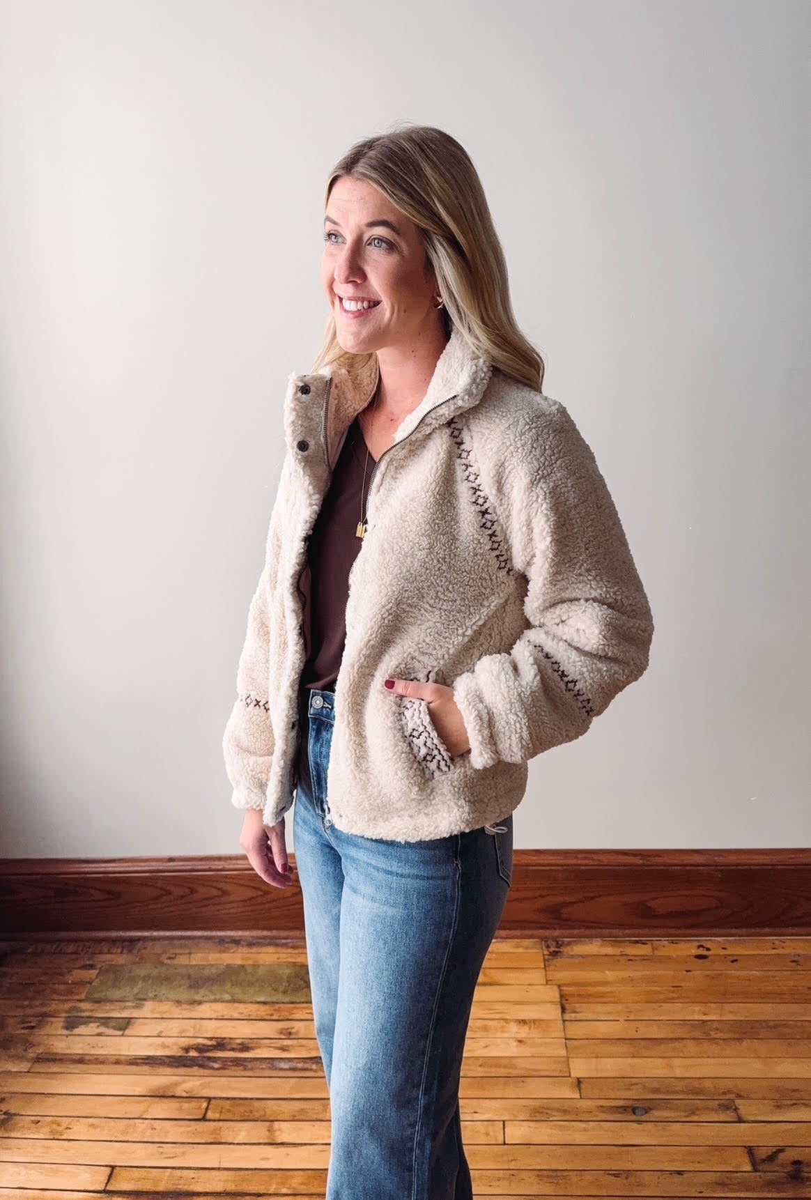 Woman wearing a beige fleece jacket with decorative buttons on a plain background
