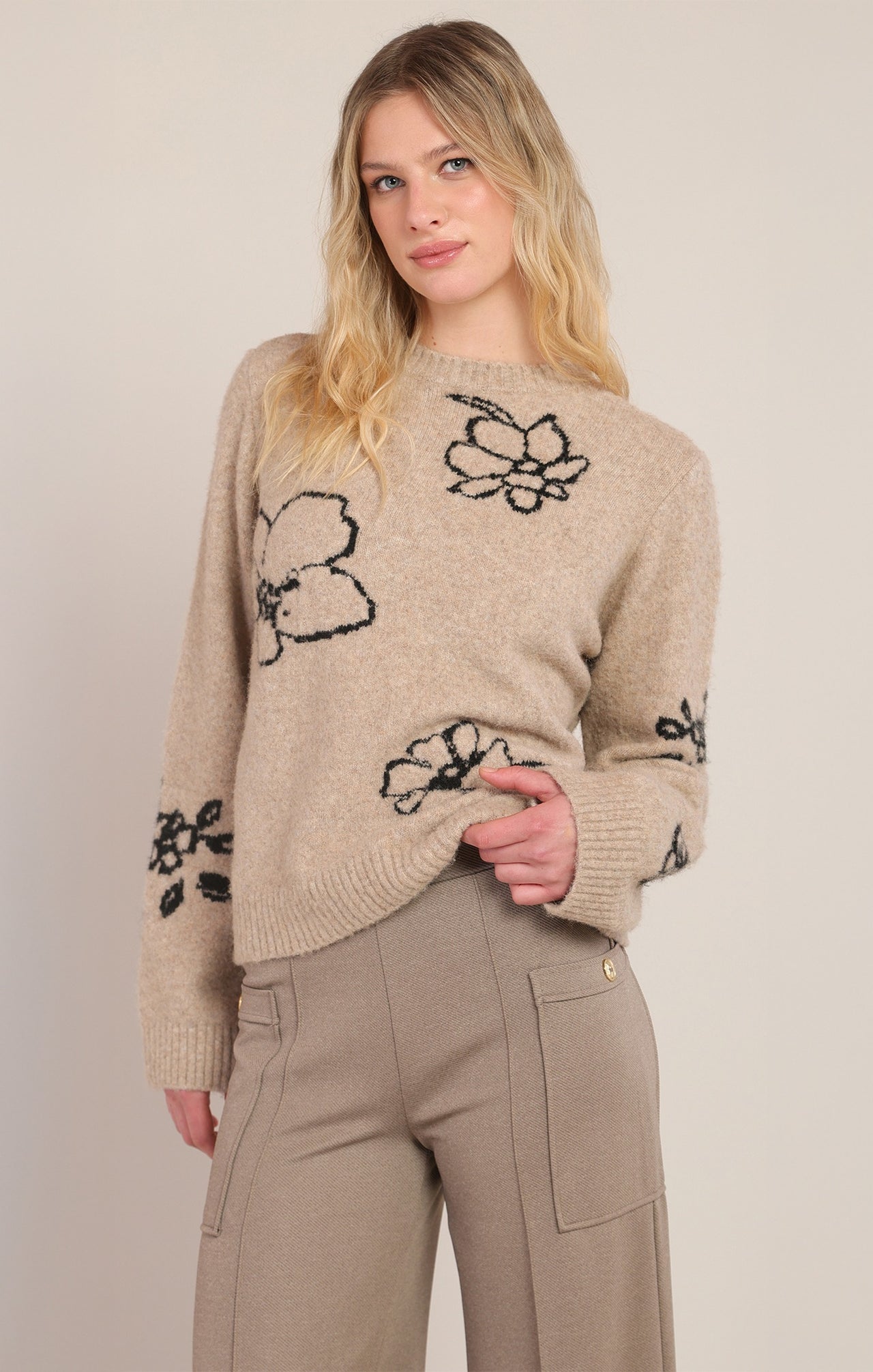 Woman wearing a beige sweater with black floral patterns on a plain background
