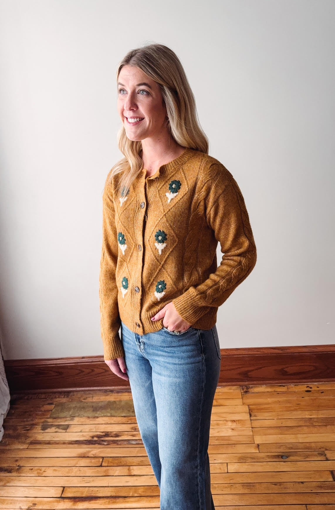 Woman wearing a mustard yellow cardigan with green buttons in a room with wooden flooring.