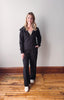 Woman wearing a black tracksuit standing on a wooden floor with a white wall background