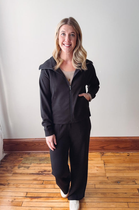 Woman wearing a black tracksuit standing on a wooden floor with a white wall background