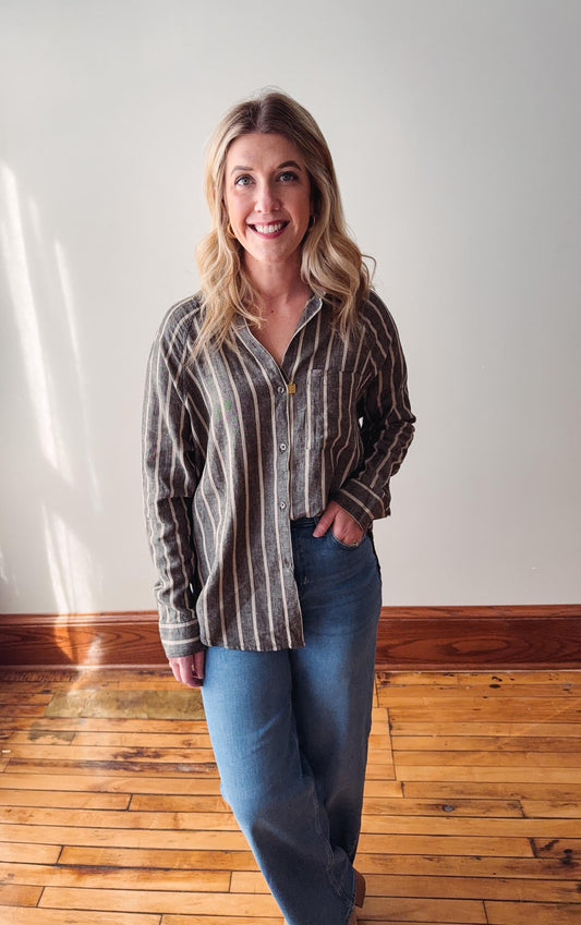 Woman wearing a striped shirt and jeans standing in a room with wooden flooring and white walls.