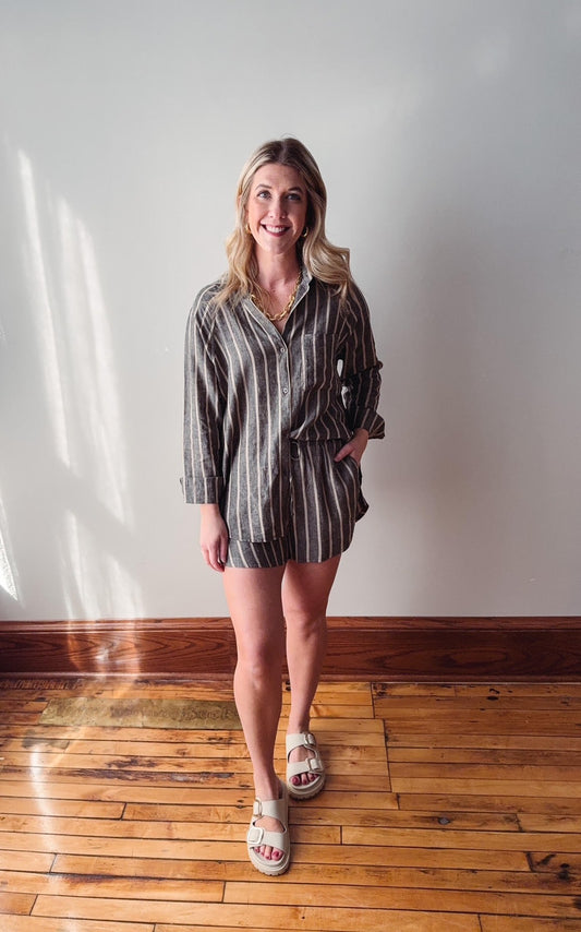 Woman standing on a wooden floor wearing a striped dress and sandals.