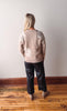 Person wearing a beige sweater with floral patterns and black pants standing on a wooden floor.