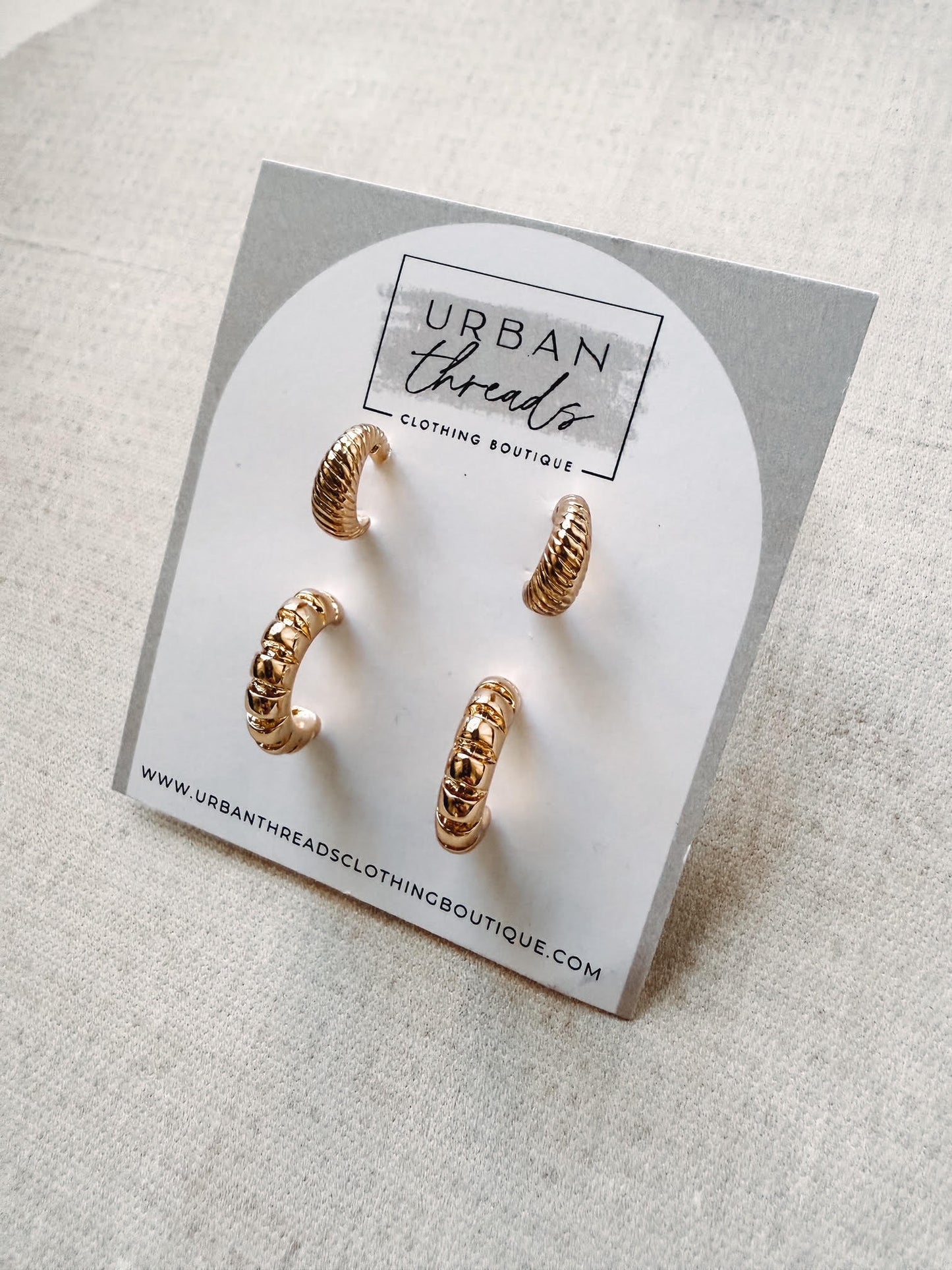 Gold hoop earrings on a 'Urban Threads' branded card against a light background