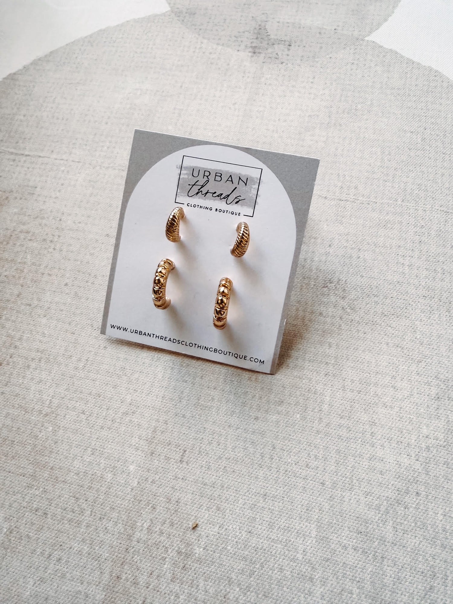 Gold hoop earrings on a branded card against a textured gray background