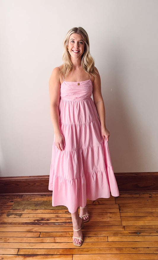 Woman wearing a pink dress standing on a wooden floor against a white wall