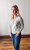 Woman wearing a light gray long-sleeve shirt with a blue collar against a white wall.