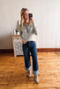 Woman taking a mirror selfie wearing a gray sweater and blue jeans in a room with wooden flooring.