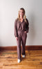 Woman wearing a brown outfit standing on a wooden floor with a white wall background