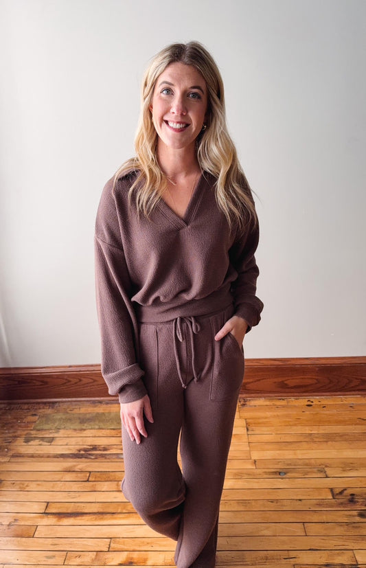Woman wearing a brown outfit standing on a wooden floor with a white wall background