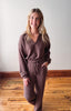 Woman wearing a brown outfit standing on a wooden floor with a white wall background