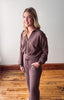 Woman wearing a brown outfit standing on a wooden floor with a white wall background